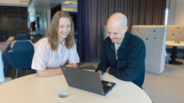 Varman vakuutushakemuksen tuoteomistaja Maria Väisänen ja käyttökokemussuunnittelija Aleksi Ruuhilahti istuvat pöydän ääressä ja katsovat hymyillen kannettavaa tietokonetta.