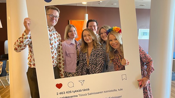 Meidän Salmisaari -projektin työryhmäläisiä yhteiskuvassa, käsissään iso instagram-kuvakehys, taustalla toimiston olohuone.