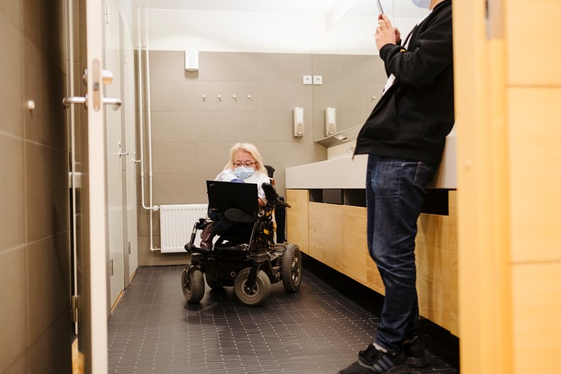 Nainen pyörätuolissa yrityksen wc-tiloissa. 